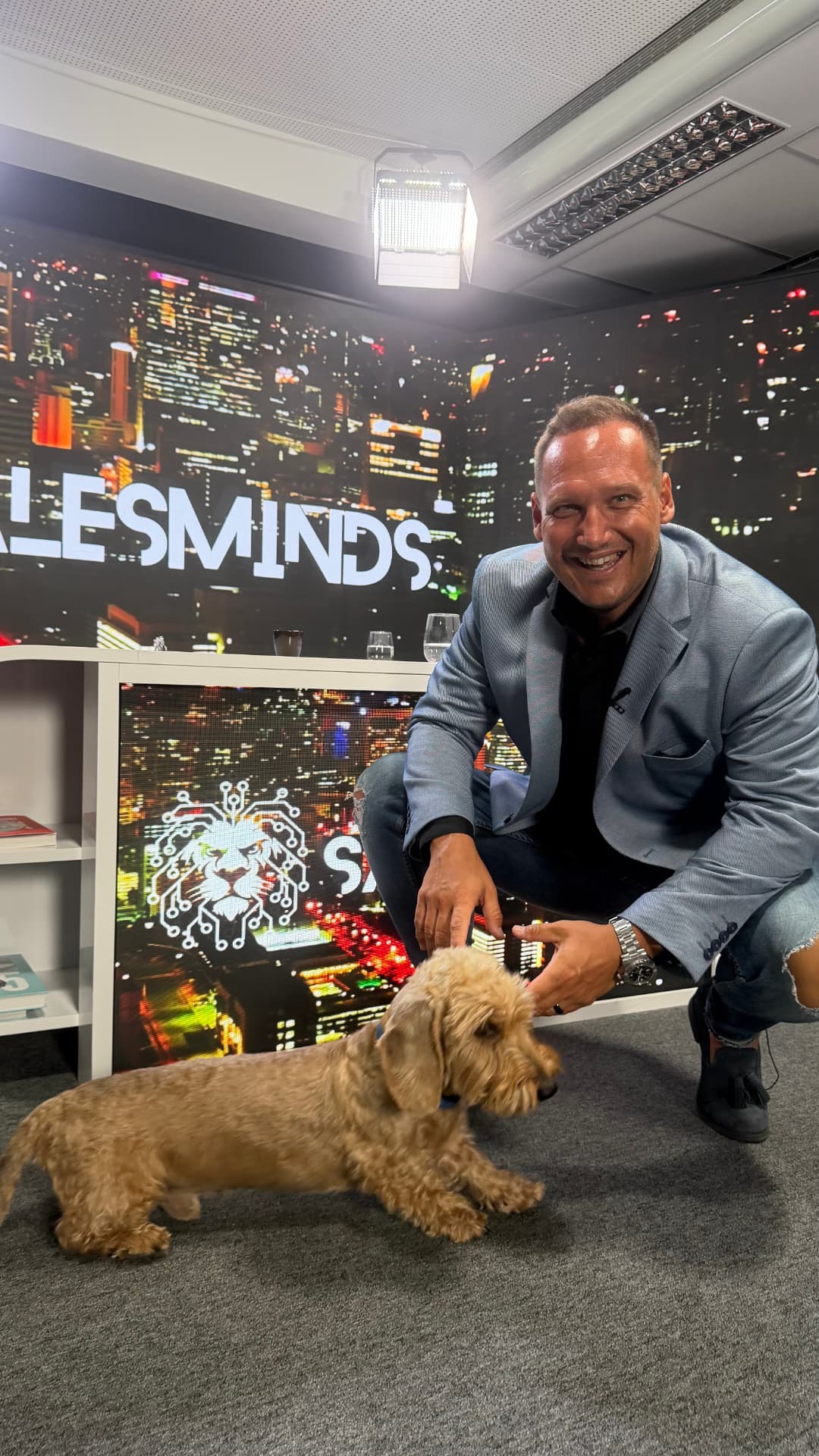 Végvári Tibor mosolyogva guggol a Sales Minds stúdióban egy kutyával